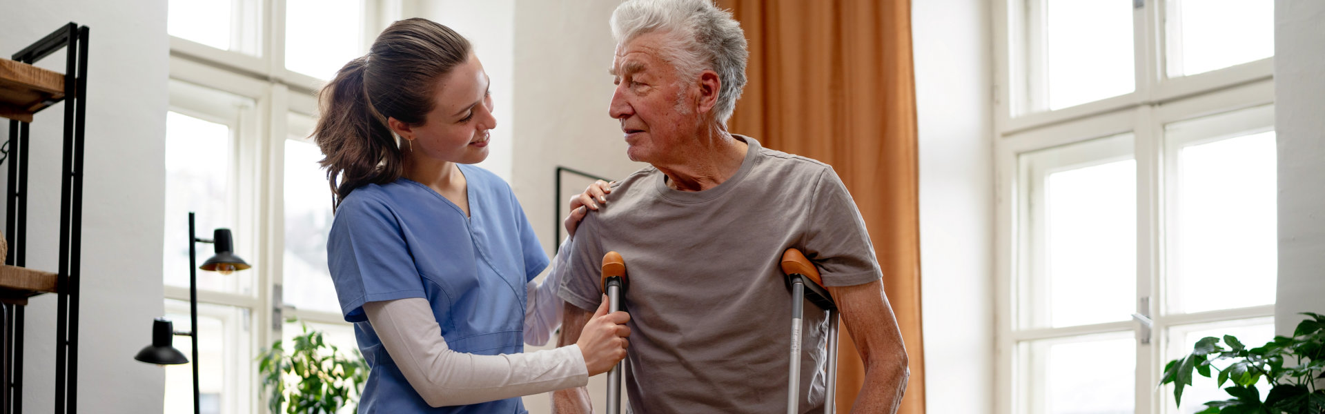 elderly in crutches assisted by his caregiver